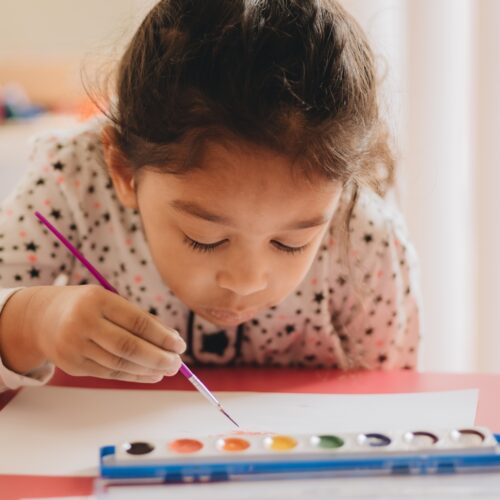 Pretty diverse pre school girl at home painting with water colors